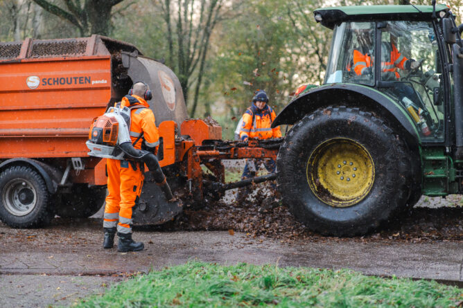 Medewerkers buitendienst met bladblazers en een tractor met aanhanger