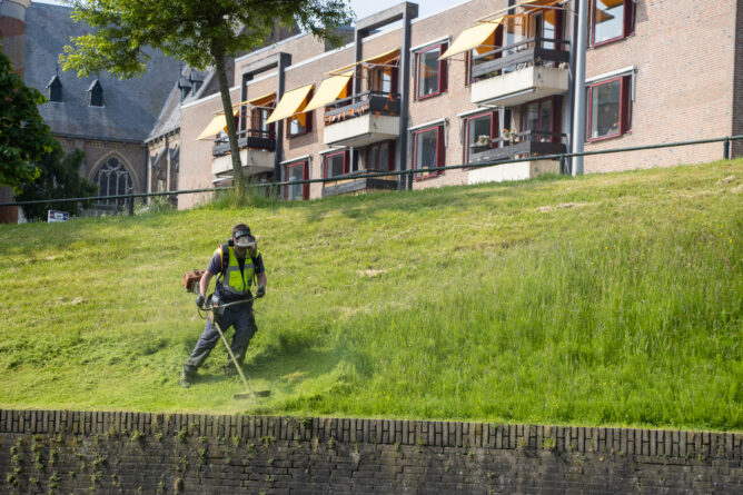 Medewerker buitendienst bezig met grasmaaien langs de kade